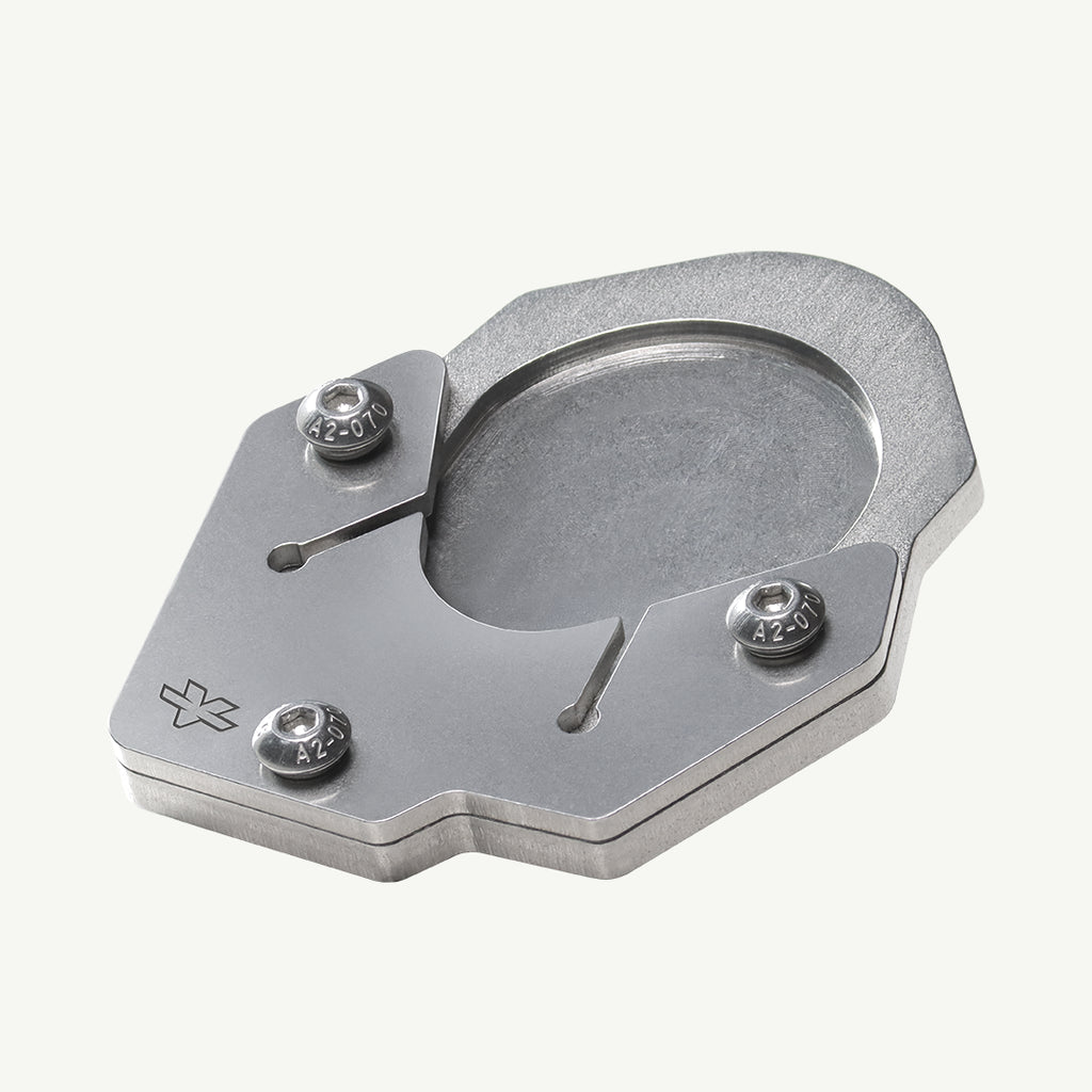 A brushed silver metal mechanical component, likely a watch movement bridge or clutch plate, featuring three hex screws and a small engraved logo, shown on a light off-white background.