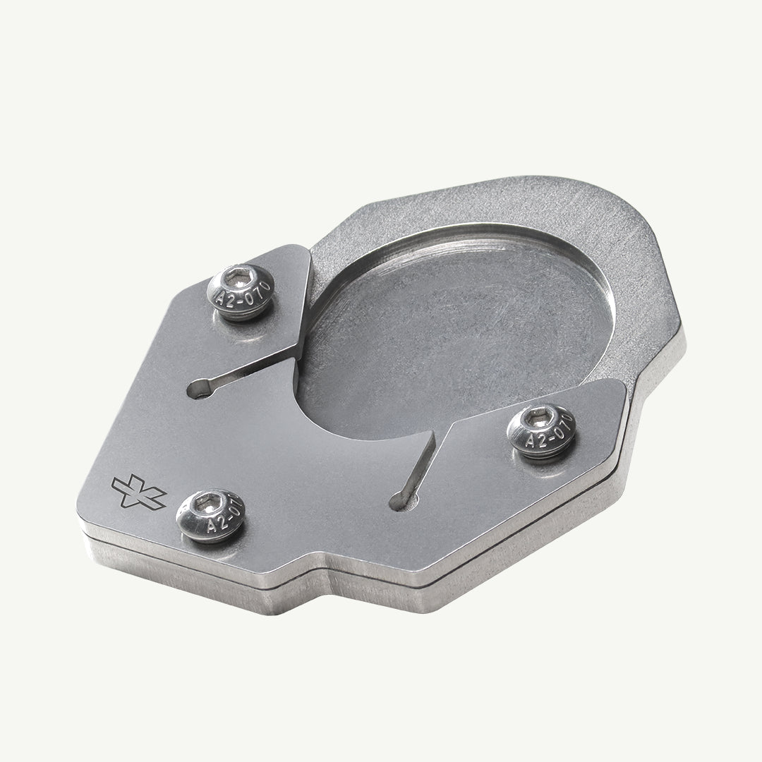 A brushed silver metal mechanical component, likely a watch movement bridge or clutch plate, featuring three hex screws and a small engraved logo, shown on a light off-white background.