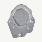 A silver metallic bicycle disc brake pad shown from a top-down view on a light off-white background. The pad features a textured outer ring, a smooth center, and two visible silver hardware screws.