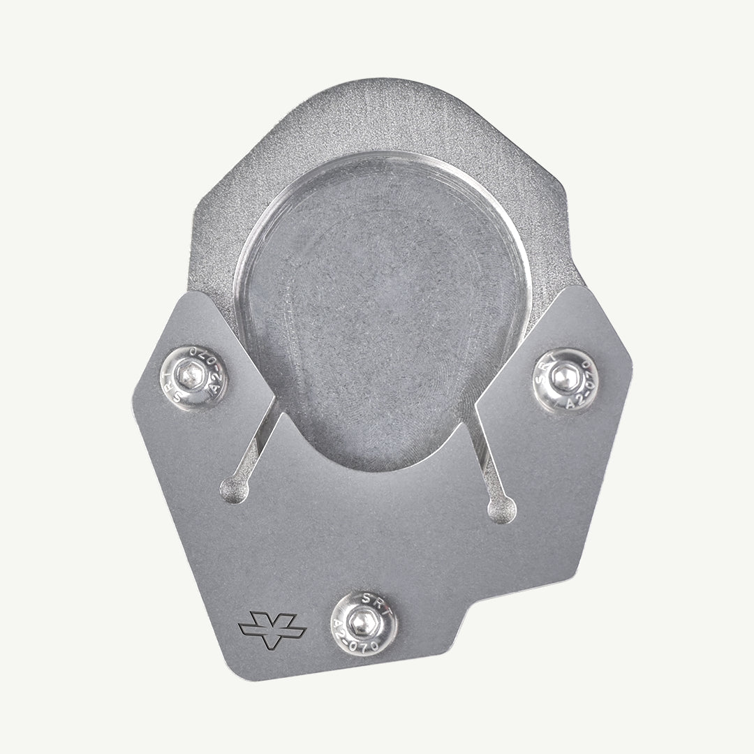 A silver metallic bicycle disc brake pad shown from a top-down view on a light off-white background. The pad features a textured outer ring, a smooth center, and two visible silver hardware screws.