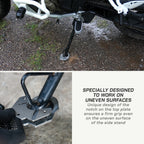 A motorcycle side stand shown outdoors on wet gravel, with a close-up detail of the foot peg and base plate. Text on the right explains that the stand is specially designed to work on uneven surfaces due to its unique notch design.