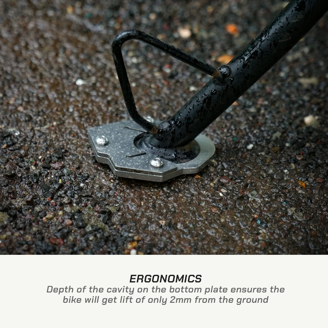 Close-up of a bicycle bottom bracket and pedal spindle mounted on wet asphalt, with text below reading 'ERGONOMICS' and a description about the bike lifting only 2mm from the ground.