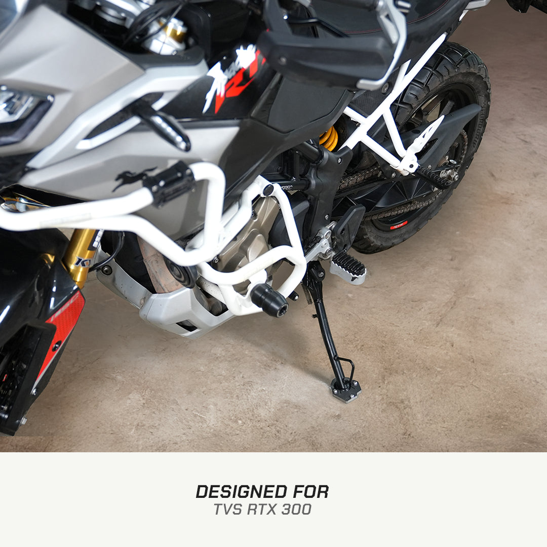 A close-up of a motorcycle's rear section showing a white protective crash bar and rear frame, with a text banner at the bottom that reads 'DESIGNED FOR TVS RTX 300'.