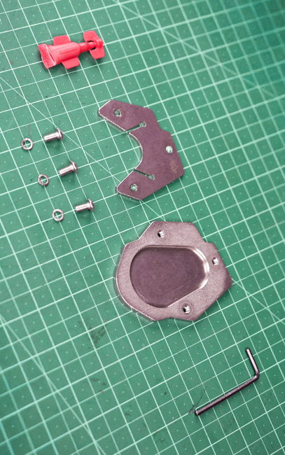 Best in class materials and components Disassembled metal components and a red plastic piece laid out on a green cutting mat with grid lines, alongside a small hex wrench.