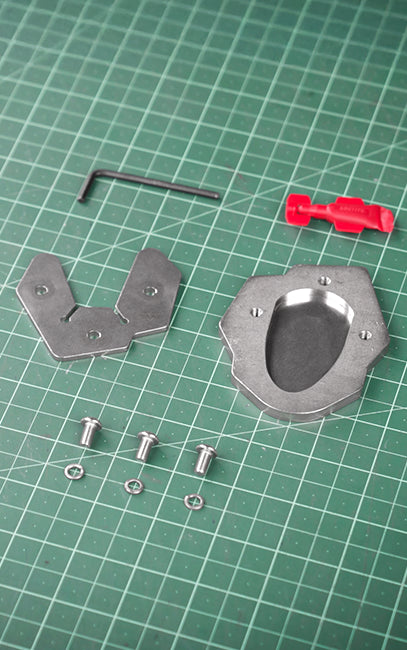 Extended footprint area Metal mechanical parts and a small red plastic piece arranged on a green gridded cutting mat, with a hex key and screws nearby.