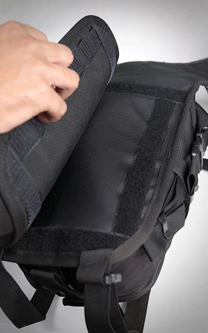 Detachable Back Pad Black tactical backpack with a hand adjusting a strap on a gray background