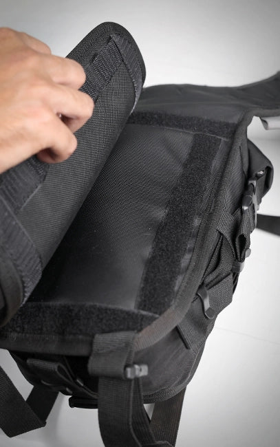 Detachable Back Pad Black tactical backpack with a hand adjusting a strap on a white background