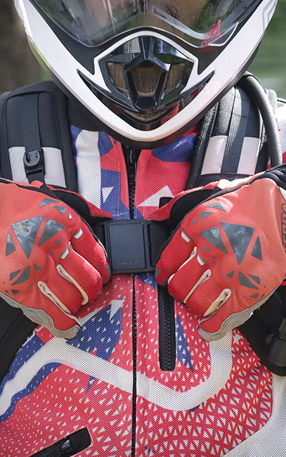 Fidlock Sternum Closure Close-up of a person wearing a red, white, and blue patterned motorcycle jacket, red gloves, and a white and black full-face helmet.