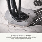 Close-up of a black and silver metal foot stand with a textured black grip, shown on a light stone surface with text below reading 'EXTENDED FOOTPRINT AREA'.
