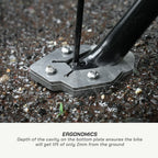 Close-up of a bicycle fork base mounted on a metal ground plate with three silver screws, set in gravel. Text below reads 'ERGONOMICS' with a description about the 2mm ground lift.