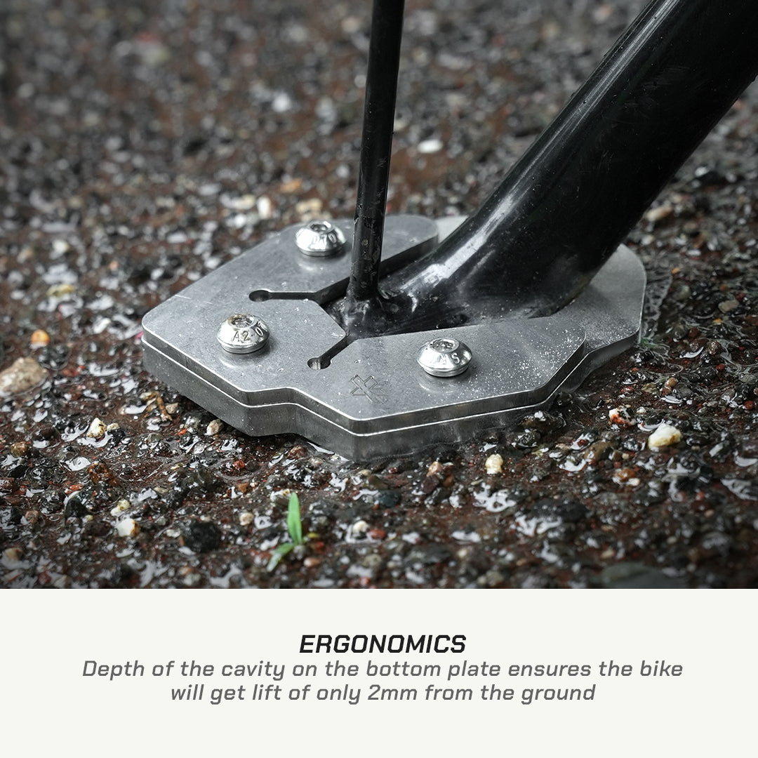 Close-up of a bicycle fork base mounted on a metal ground plate with three silver screws, set in gravel. Text below reads 'ERGONOMICS' with a description about the 2mm ground lift.