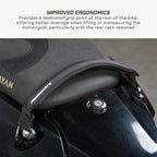 color_black Close-up of a black motorcycle seat pad with a textured grip point and a strap attachment, shown on a motorcycle with text at the top describing improved ergonomics.