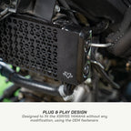 color_black Close-up of a black motorcycle accessory mounted over a radiator, with text at the bottom reading 'PLUG & PLAY DESIGN' and 'Designed to fit the XSR155 YAMAHA without any modification, using the OEM fasteners.'.