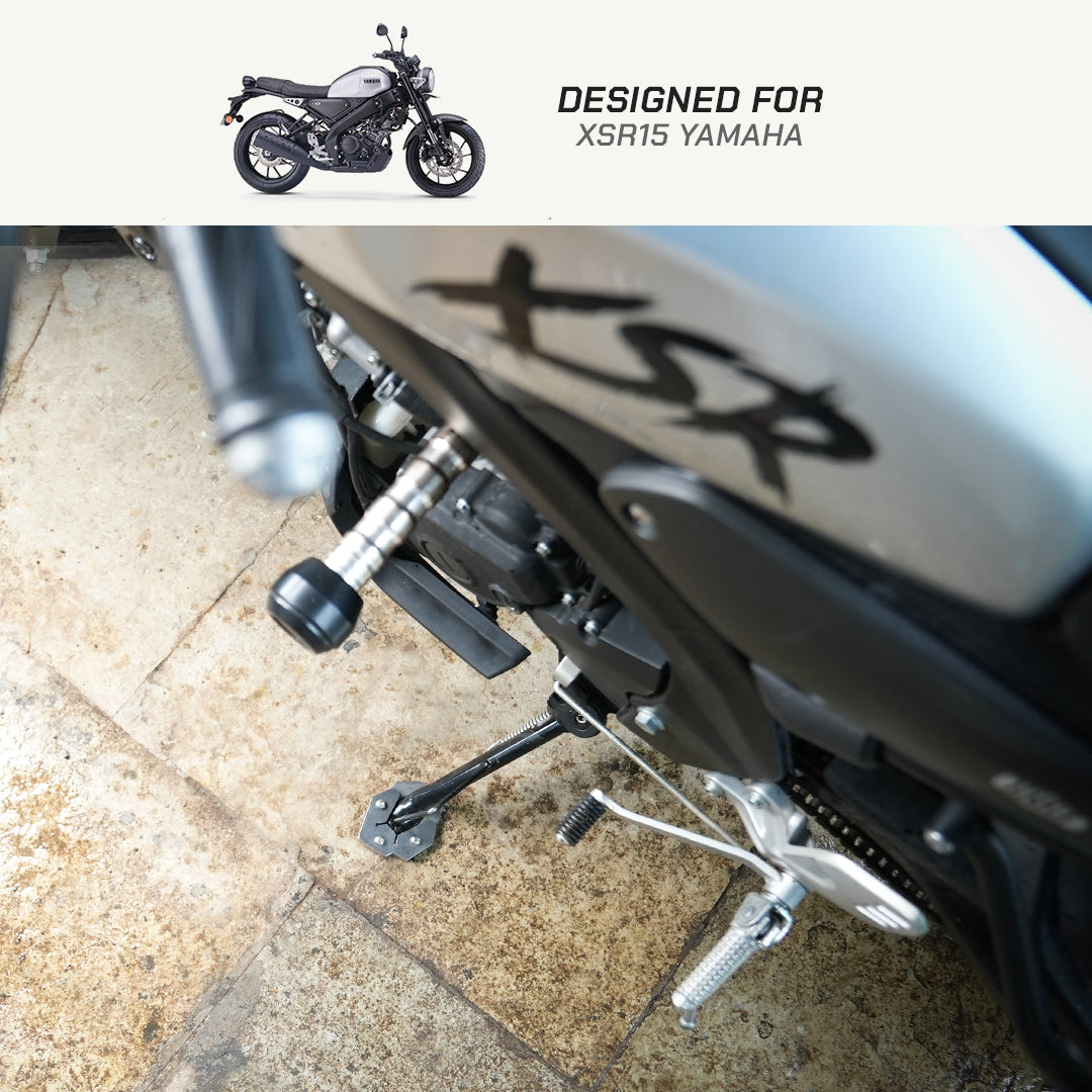 Close-up of a motorcycle's rear section with foot pegs and exhaust, shown on a stone floor. A small inset at the top shows a full view of a black and silver Yamaha XSR15 motorcycle with the text 'DESIGNED FOR XSR15 YAMAHA'.