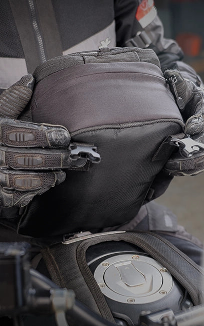 High Tenacity Polyester at the base panel enhances durability in high-contact areas and supports long-term structural stability. Close-up of a person wearing gloves and a jacket with a motorcycle seat and engine cover in the background.