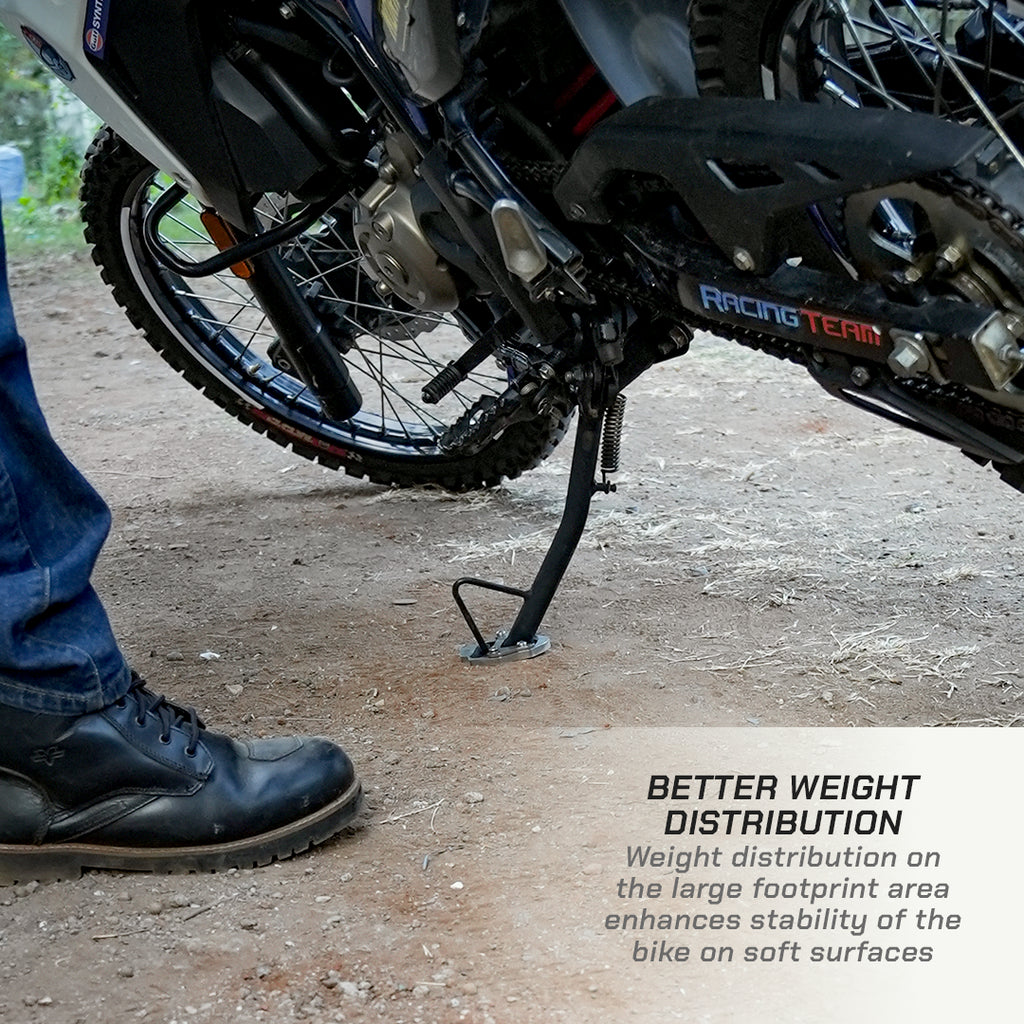 color_common Motorcycle with a foot peg and person wearing boots on a dirt surface, emphasizing stability.