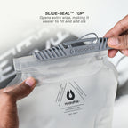 A clear HydroPak hydration pouch being held by two hands, with a gray slide-seal closure at the top. Text at the top reads 'SLIDE-SEAL TOP' and 'Opens extra wide, making it easier to fill and add ice.
