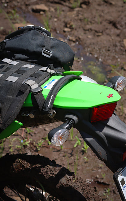 Improved ergonomics A close-up outdoor shot of a bright green motorcycle rear section with a black luggage rack and black backpack mounted on the back, set against muddy ground.