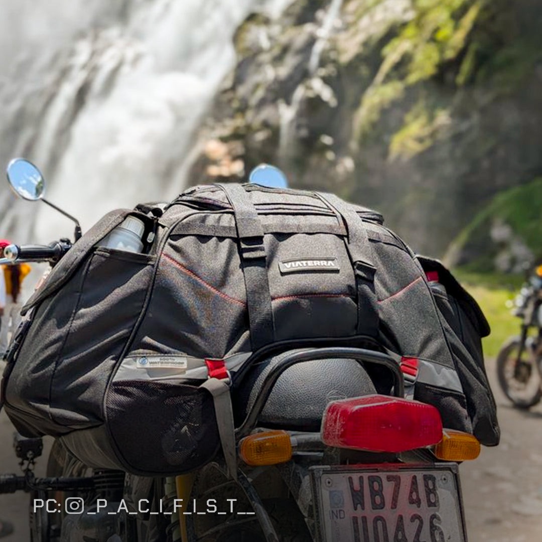 Motorcycle with a large backpack on a scenic road with a waterfall in the background