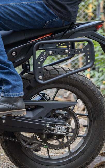 Pillion Friendly Close-up of a motorcycle with a luggage rack, showing a person wearing blue jeans and black shoes.