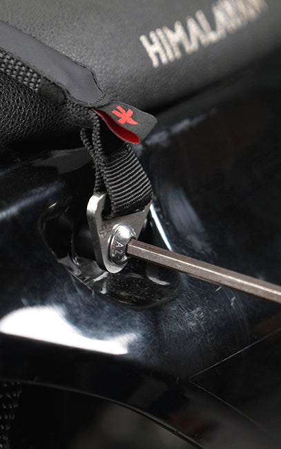 Plug & Play design Close-up of a black zippered pouch with a red logo tab, attached to a black strap and secured with a metal toggle and screwdriver, on a dark glossy surface. The word HIMALAYA is partially visible on the pouch.