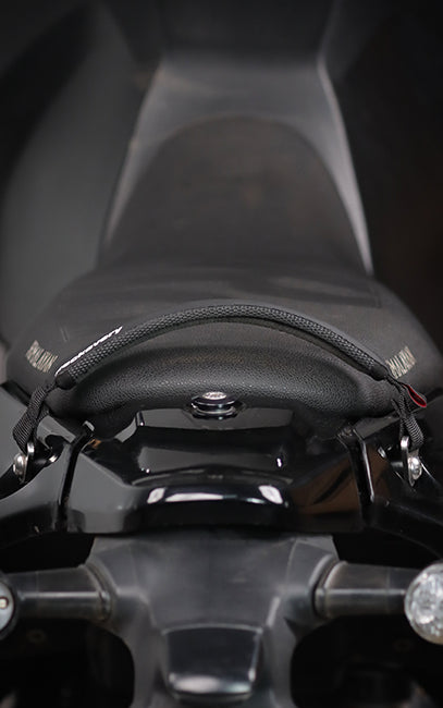 Precision & Consistency A close-up shot of a black motorcycle seat with a textured grip strap across the middle, mounted on a glossy black motorcycle frame.