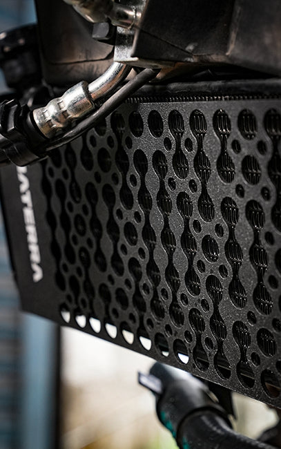 Precision & Consistency Close-up of a black perforated metal panel with a repeating circular cutout pattern, attached to a dark industrial frame with visible hoses and metal components.