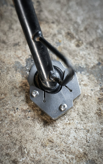 Precision & ConsistencyClose-up of a black metal mounting pole secured to a textured concrete surface with a silver hexagonal base plate and three visible screws.
