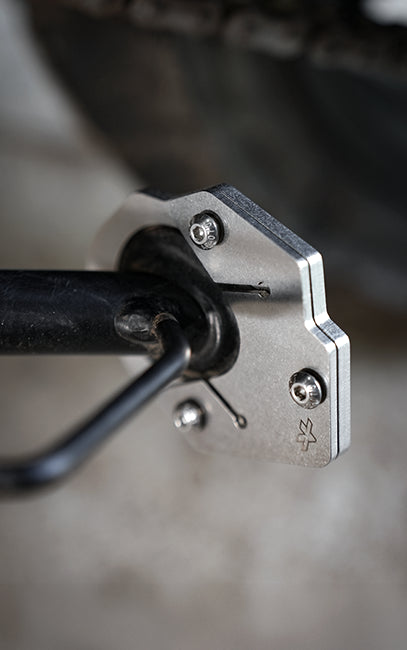 Premium build and finish Close-up of a silver metal bicycle fork end with black fork tubes and threaded bolts, photographed outdoors with a blurred background.