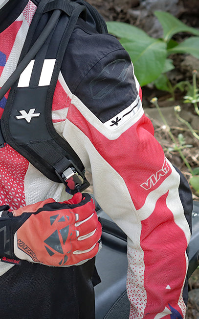 Quick On, Quick Off Close-up of a red, white, and black motorcycle jacket with a black backpack and a red glove, worn by a person outdoors with green foliage in the background.