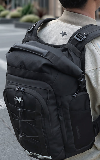 DASH System (Dual Adjustable Sliding Harness) A black tactical-style backpack with multiple zippered compartments and a roll-top closure, shown worn on a person from behind in an outdoor urban setting.