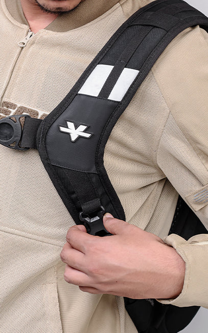 Quick Release Harness Buckle Close-up of a person wearing a black backpack strap over a beige zip-up jacket, with the strap featuring white reflective stripes and a white stylized logo.