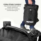 A black tactical-style backpack with a reinforced handle is shown being carried by a person in jeans and boots, with a close-up of the handle in the foreground. Text on the left reads 'FORM-STABLE HANDLE Reinforced handle with a shape-retaining structure for a secure, comfortable grip.