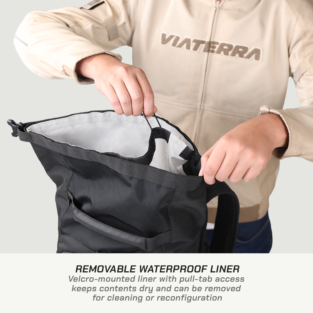 A person wearing a beige Viaterra jacket demonstrates a black waterproof bag with a removable liner. The person is shown pulling the black elastic band of the liner, which has a Velcro attachment, off the top of the bag.