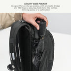 Close-up of a black backpack with a hand inserting a black umbrella into a utility side pocket, with explanatory text at the top about the side pocket design.