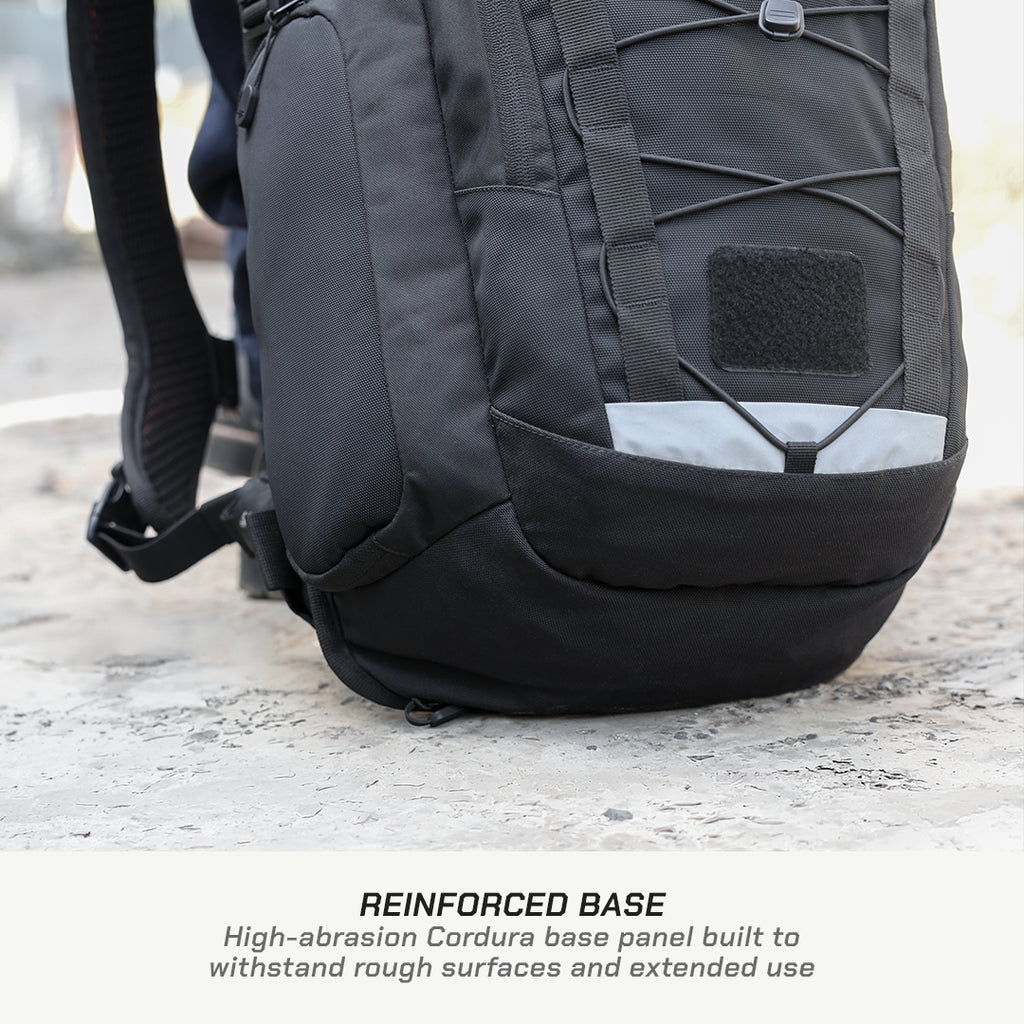 A close-up of a black backpack showing its reinforced base panel and front pocket, with a text overlay at the bottom reading 'REINFORCED BASE High-abrasion Cordura base panel built to withstand rough surfaces and extended use'.