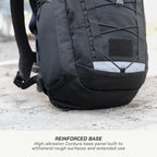 A close-up of a black backpack showing its reinforced base panel and front pocket, with a text overlay at the bottom reading 'REINFORCED BASE High-abrasion Cordura base panel built to withstand rough surfaces and extended use'.