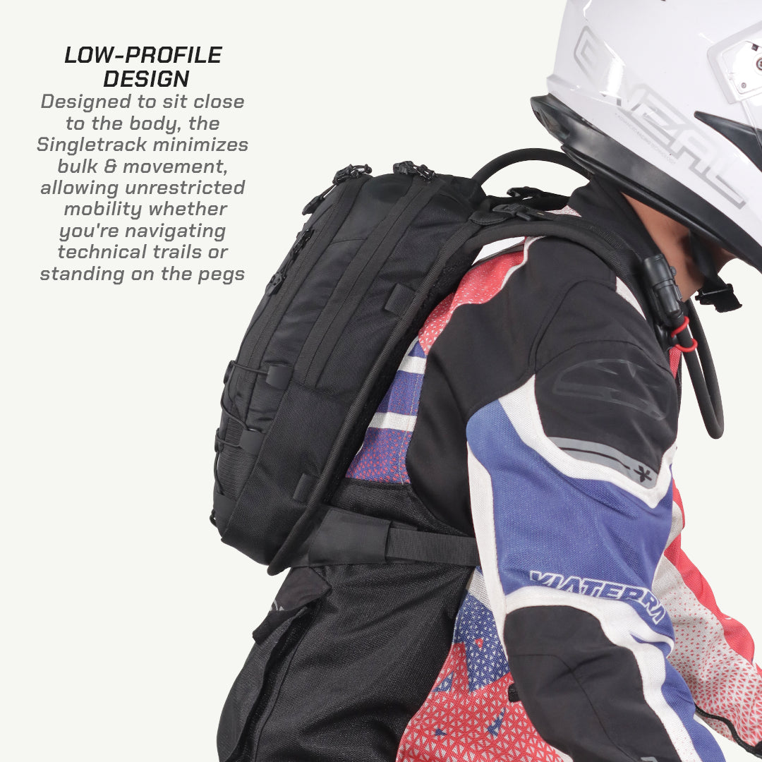 A black motorcycle backpack shown on a rider wearing a white helmet and a red, white, and blue riding jacket. The image includes text on the left explaining the low-profile design of the Singletrack backpack.