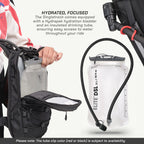 A close-up product shot showing a black hydration backpack with an open side pocket holding a translucent hydration bladder, alongside a separate Elite DSL 2L insulated drinking tube bladder. Text on the image describes the Hydrapak hydration bladder and insulated tube, with a note at the bottom mentioning the subject to availability for the tube clip color.