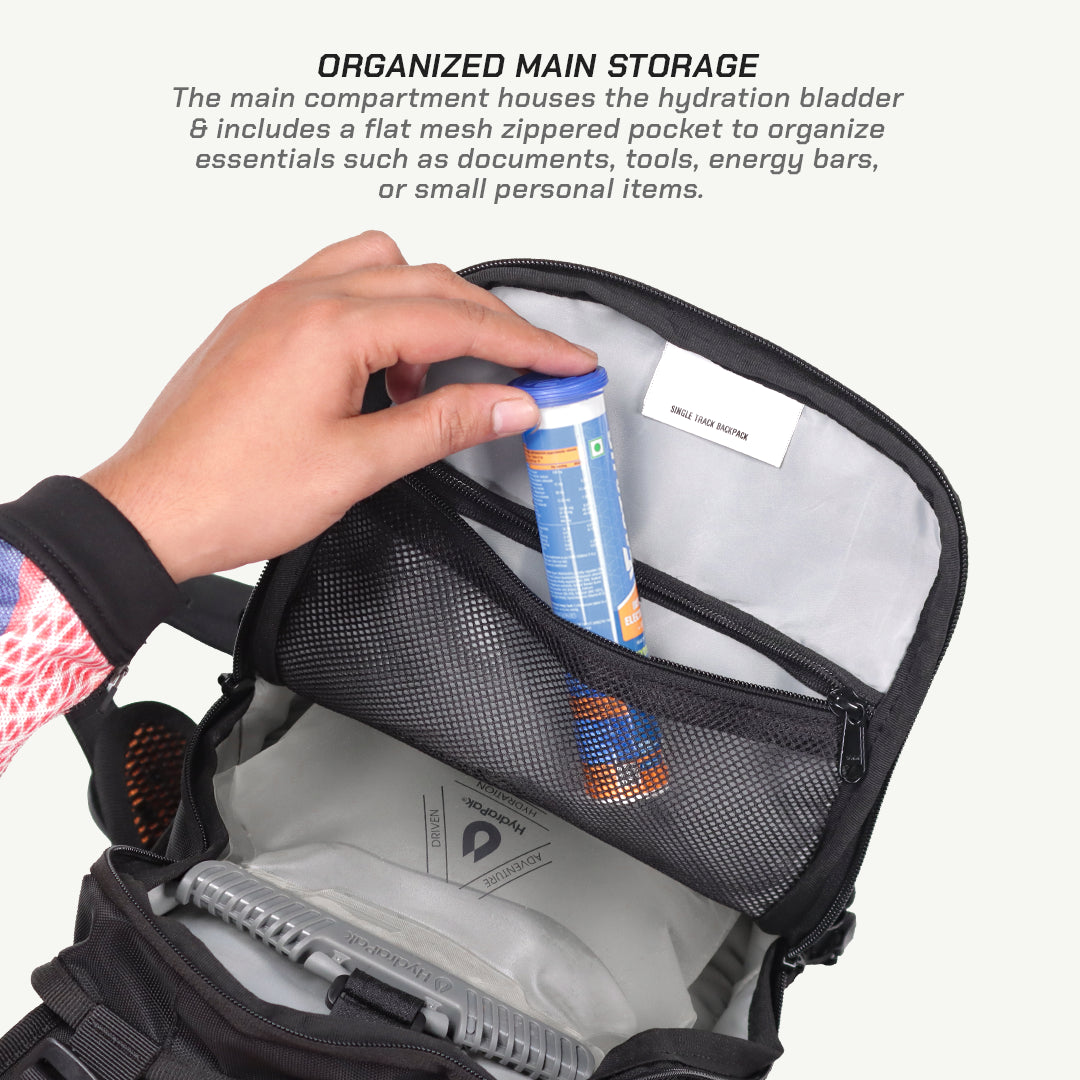 An open black and gray hydration backpack shown with a hand placing a blue and orange hydration bladder into the main compartment. The image includes descriptive text at the top about organized main storage.