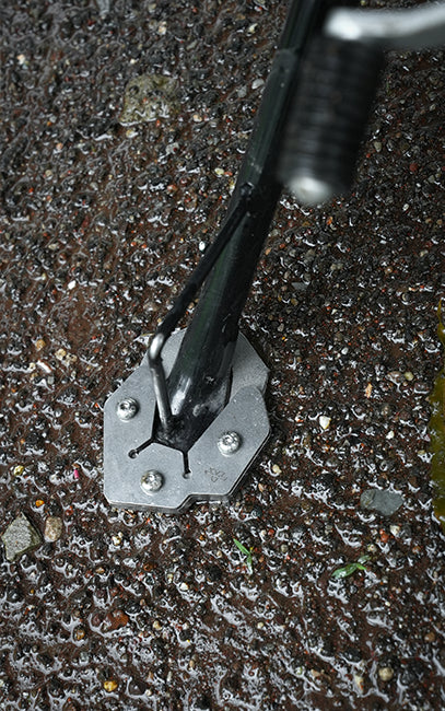 Ergonomics A close-up of a black and silver metal ground anchor or anchor tool with a hexagonal base, shown inserted into wet, muddy ground.