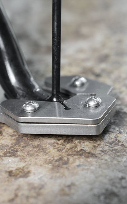 Strong clamping of shoe Close-up of a metal tool with a hexagonal silver base and black handle, resting on a textured stone surface.
