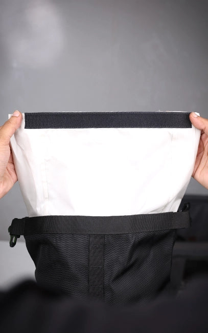Waterproof Roll-Top System Close-up of a person holding up a white garment with black trim against a gray background