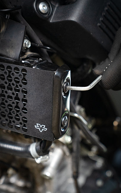 Premium build and finish Close-up of a black motorcycle engine cover with a silver hex key inserted into a mounting bolt, surrounded by engine components.